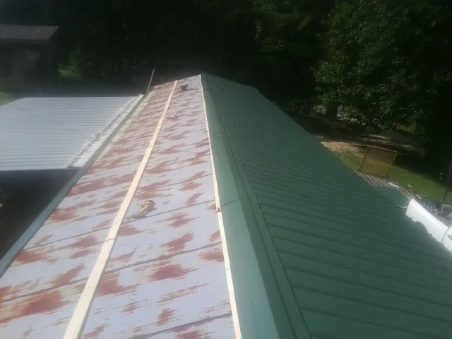 Old rusted panels beside newly installed green metal roofing — Wind Damage Roof Repair by Roofing Brothers in Nelsonville